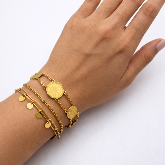 Hand wearing multiple 21k gold bracelets on a white background