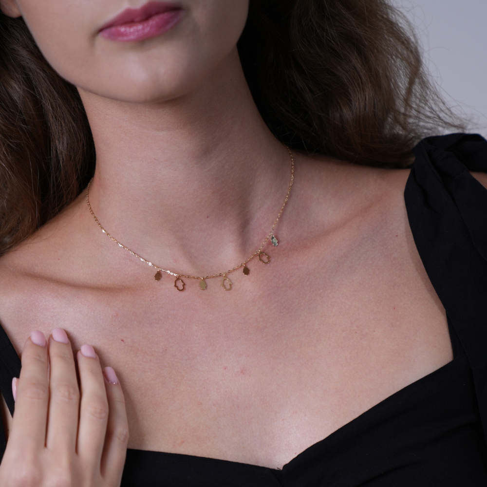 A close-up of a woman wearing a delicate gold chain necklace with small dangling oval charms, paired with a black off-the-shoulder top.