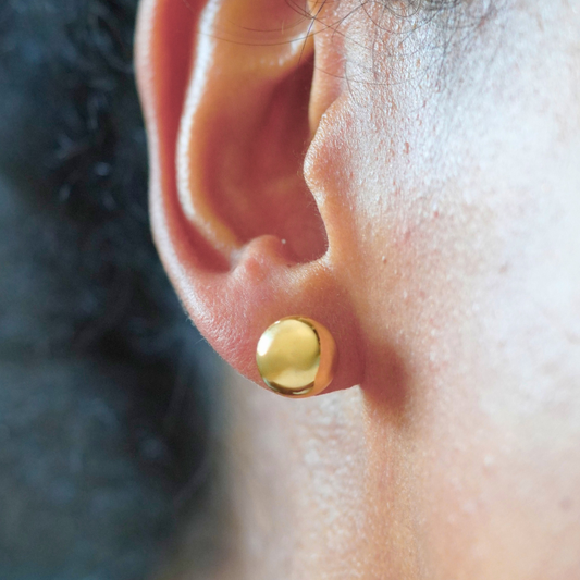 Close-up of a gold earring worn on an ear with a blurred background