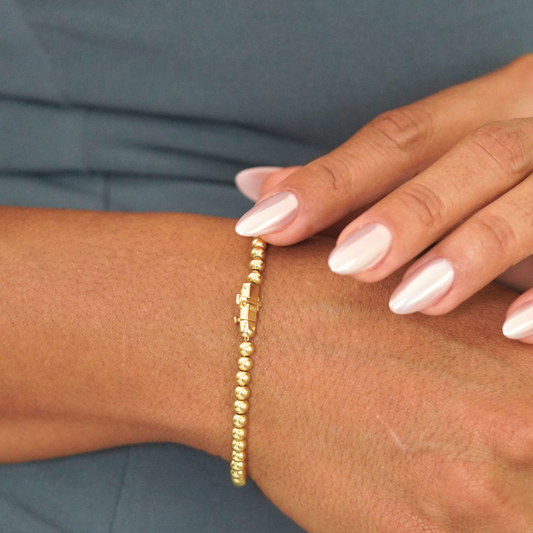 Gold beaded bracelet on a wrist with a neutral background