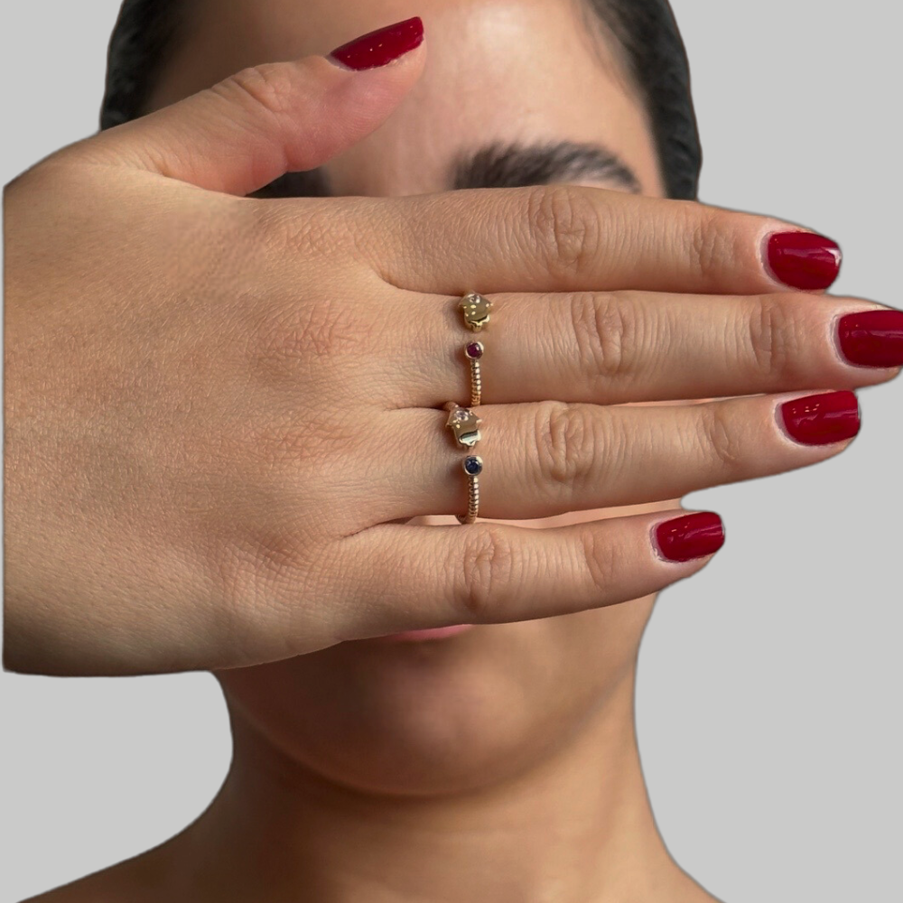A gold cuff ring with a hamsa charm and a sparkling zircon stone on a person's hand.