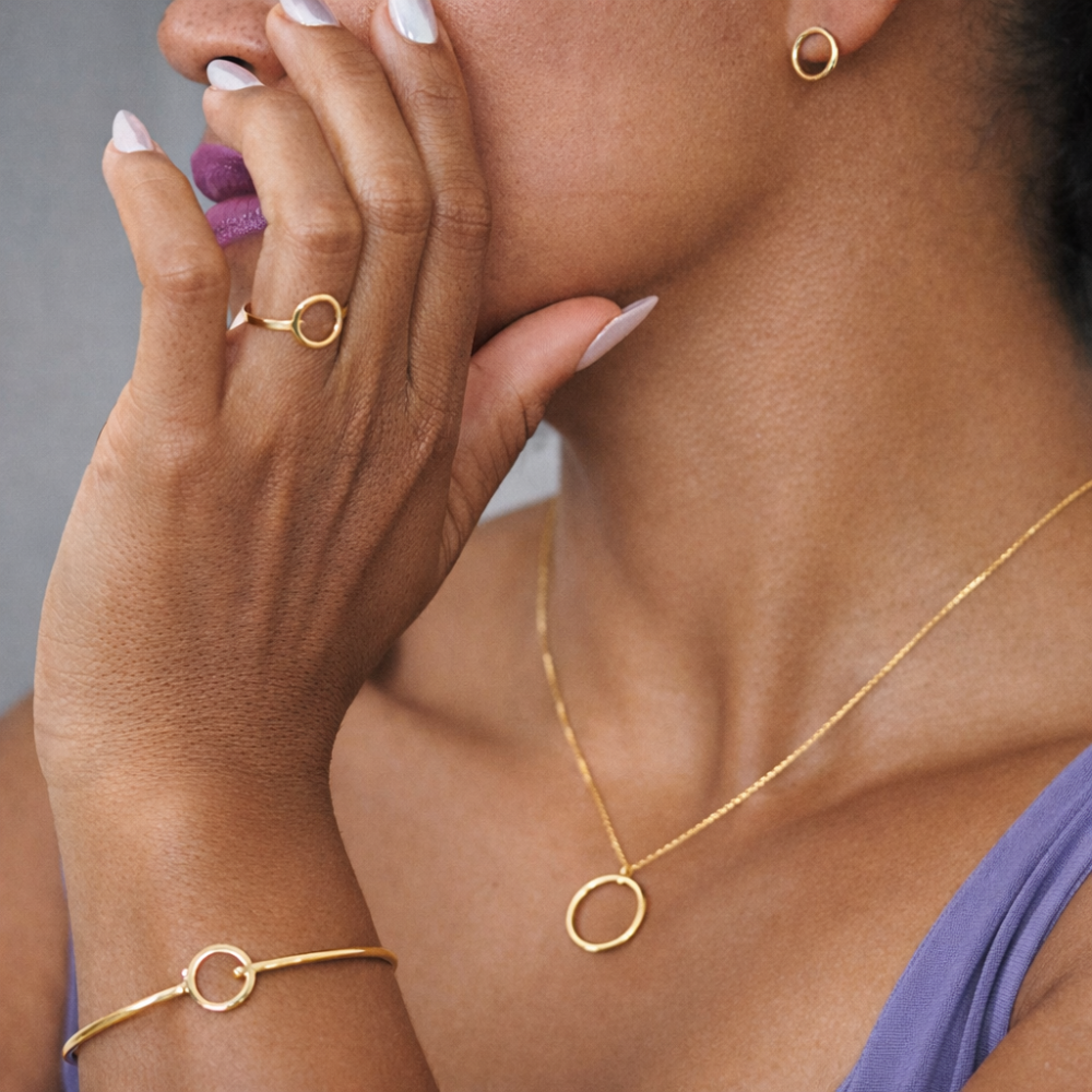 Close-up of a person wearing gold jewelry including a necklace, ring, and bracelet.