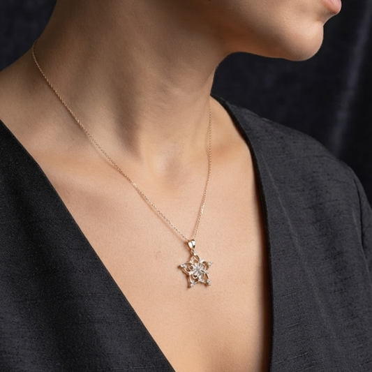 A close-up of a model wearing a delicate rose gold chain necklace with a starburst-shaped pendant set with small clear stones, paired with a black V-neck top.