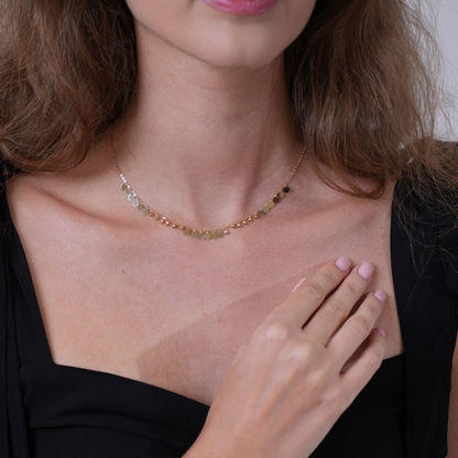 A delicate gold chain necklace with small round beads and a clear faceted gemstone, worn by a model in a black top. Circles charm gold – small necklace