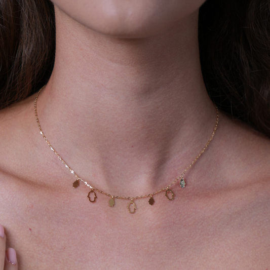 A delicate gold chain necklace with small dangling oval and circular charms, worn on a model's neck. Hands charms gold – small necklace