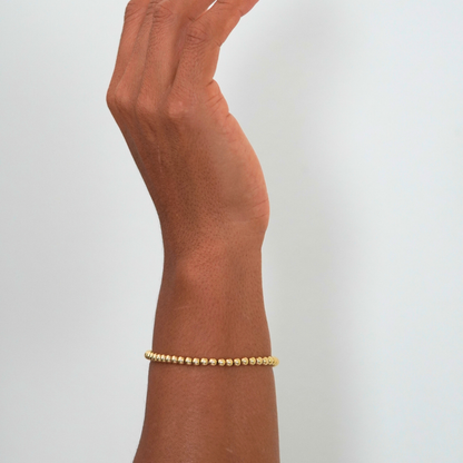 Gold bracelet on a wrist against a light gray background