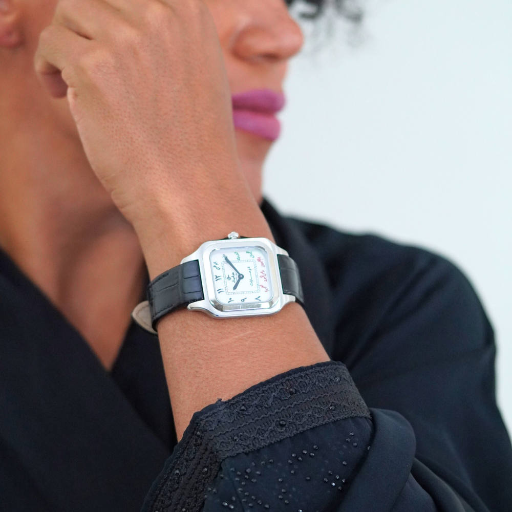 7 Emirates the Watch. Person wearing a square-shaped watch with a black strap and white face.