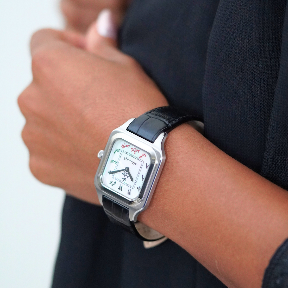 7 Emirates the Watch. Person wearing a square-faced watch with a black strap on a neutral background