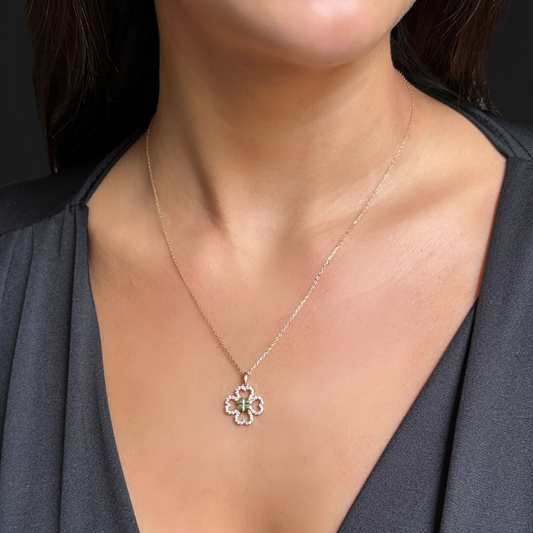 A close-up of a model wearing a delicate gold chain necklace with a four-petal flower pendant featuring a green center and small clear stones.