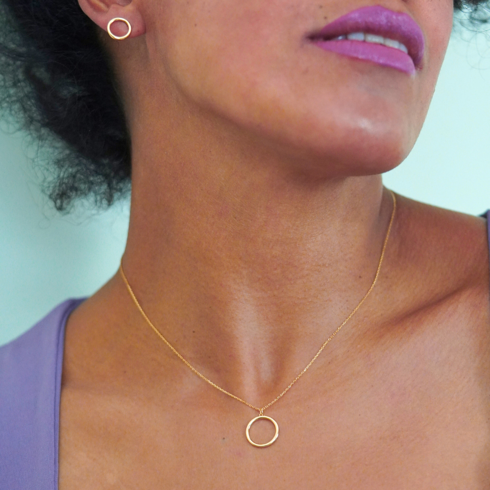 Close-up of a person wearing a gold necklace with a circular pendant.