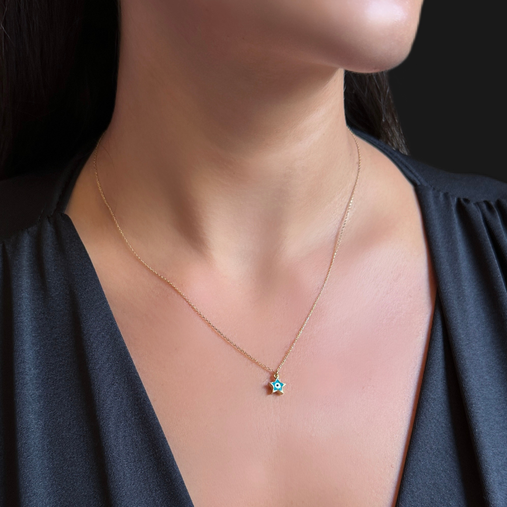A close-up of a model's neck and chest wearing a delicate gold chain necklace with a small star-shaped pendant featuring a turquoise blue center.